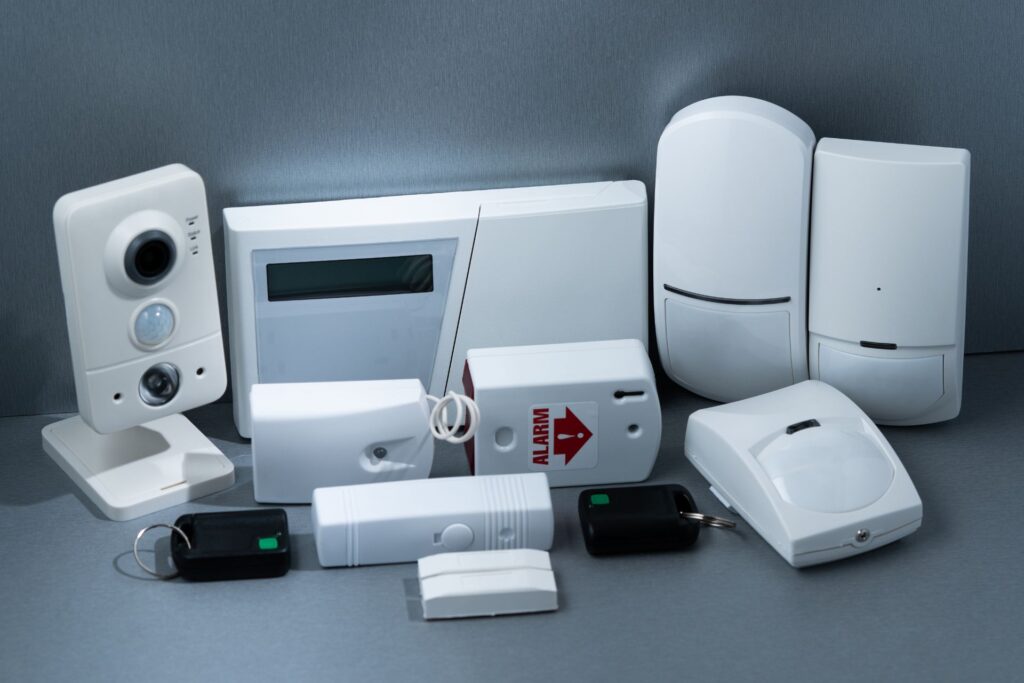 Assortment of home security devices including alarm keypads, motion detectors, and cameras, showcasing a complete alarm system setup
