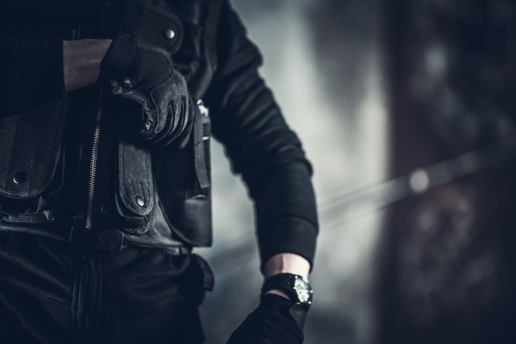 Close-up of a tactical security guard dressed in black, with focus on his gloved hands adjusting a timepiece, symbolizing precision and readiness in security operations
