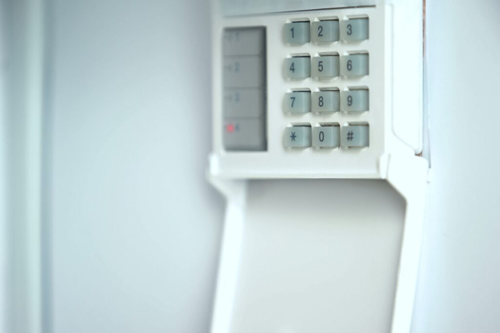 Close-up view of a home security alarm keypad open on a wall, displaying numbered buttons for system activation and deactivation.