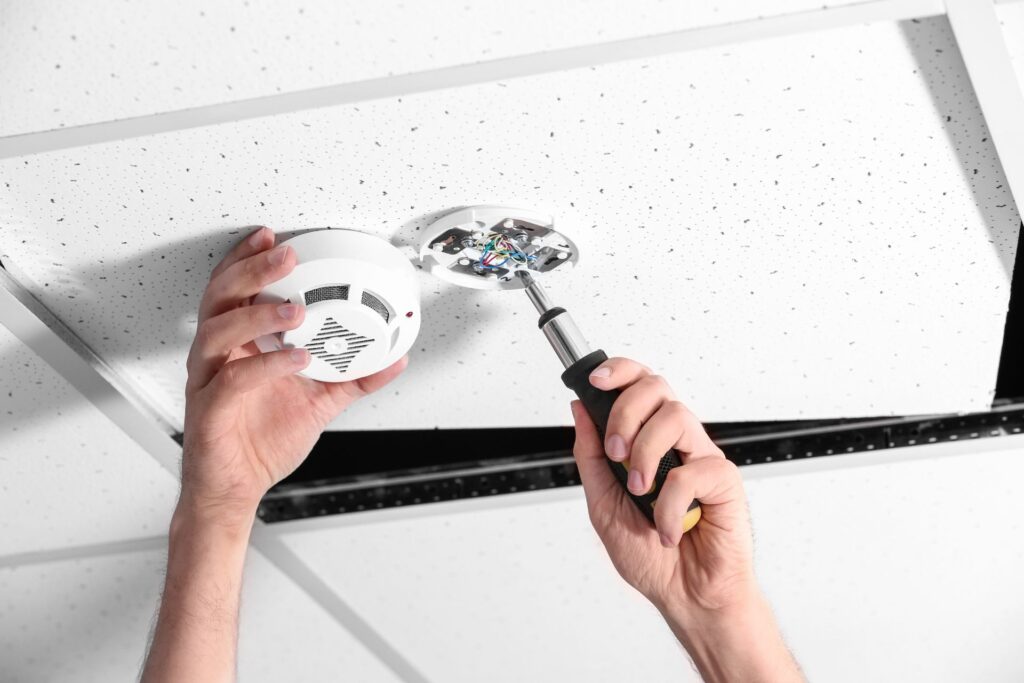 Hand of a person installing a modern smoke detector on a ceiling, illustrating DIY alarm system setup