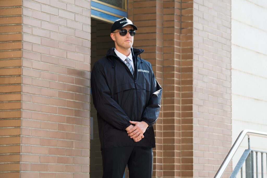 Security guard standing vigilantly at his post outside a building in Pretoria, dressed in a black jacket and cap with 'SECURITY' visibly branded on the front