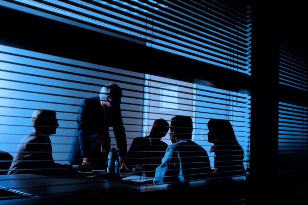 Security professionals in a dark, shadowed meeting room with blinds, discussing strategic operations for urban safety in Pretoria
